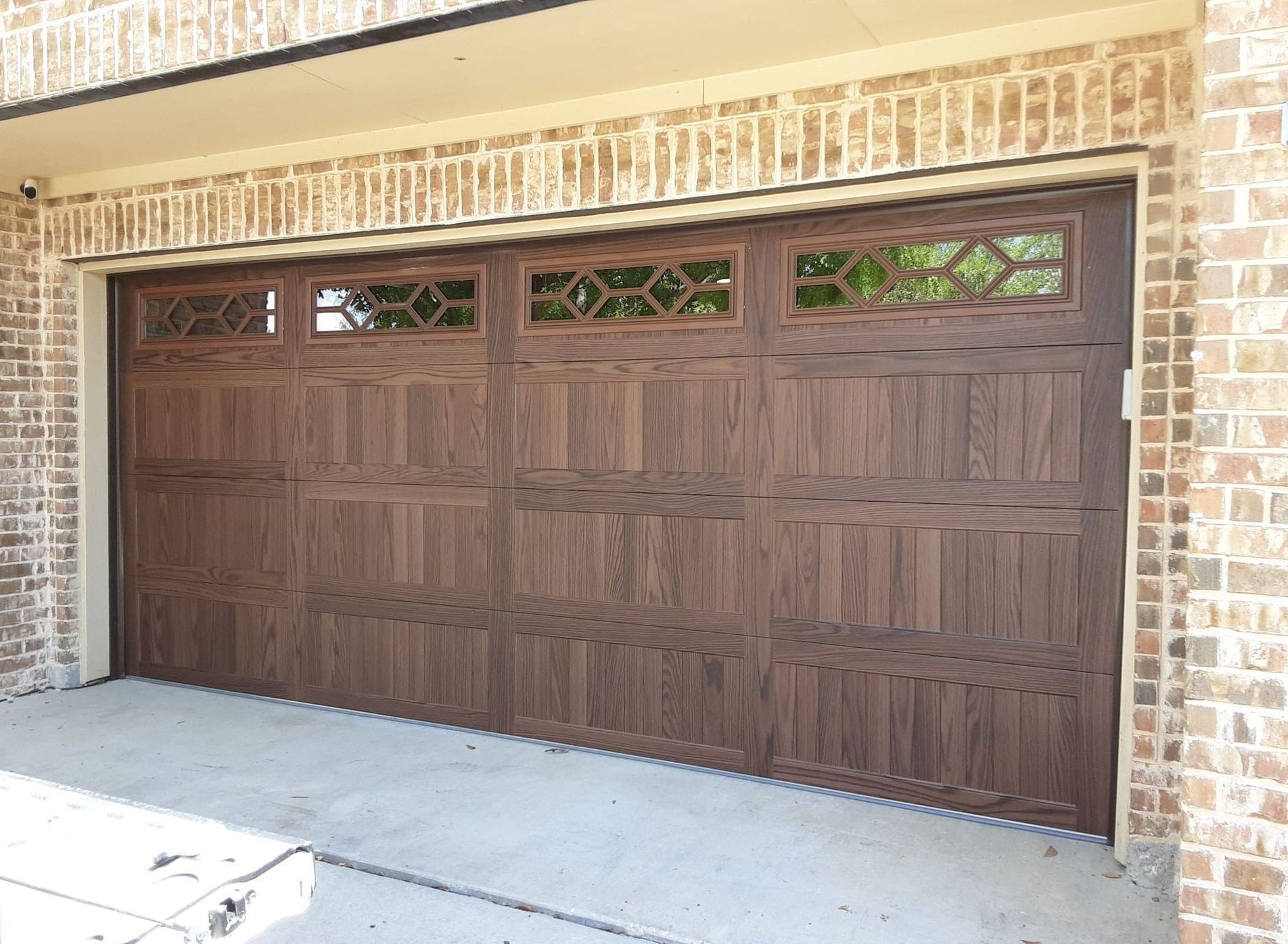 Brown garage door with decorative glass panels set in a brick frame.