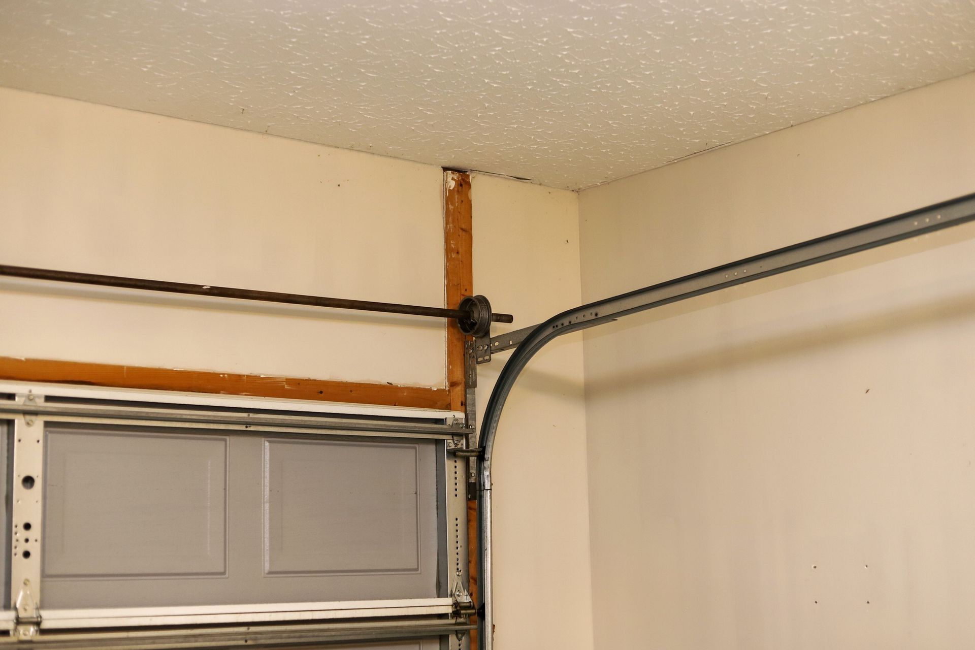 Garage door track and opener components on a beige wall, next to the garage door.
