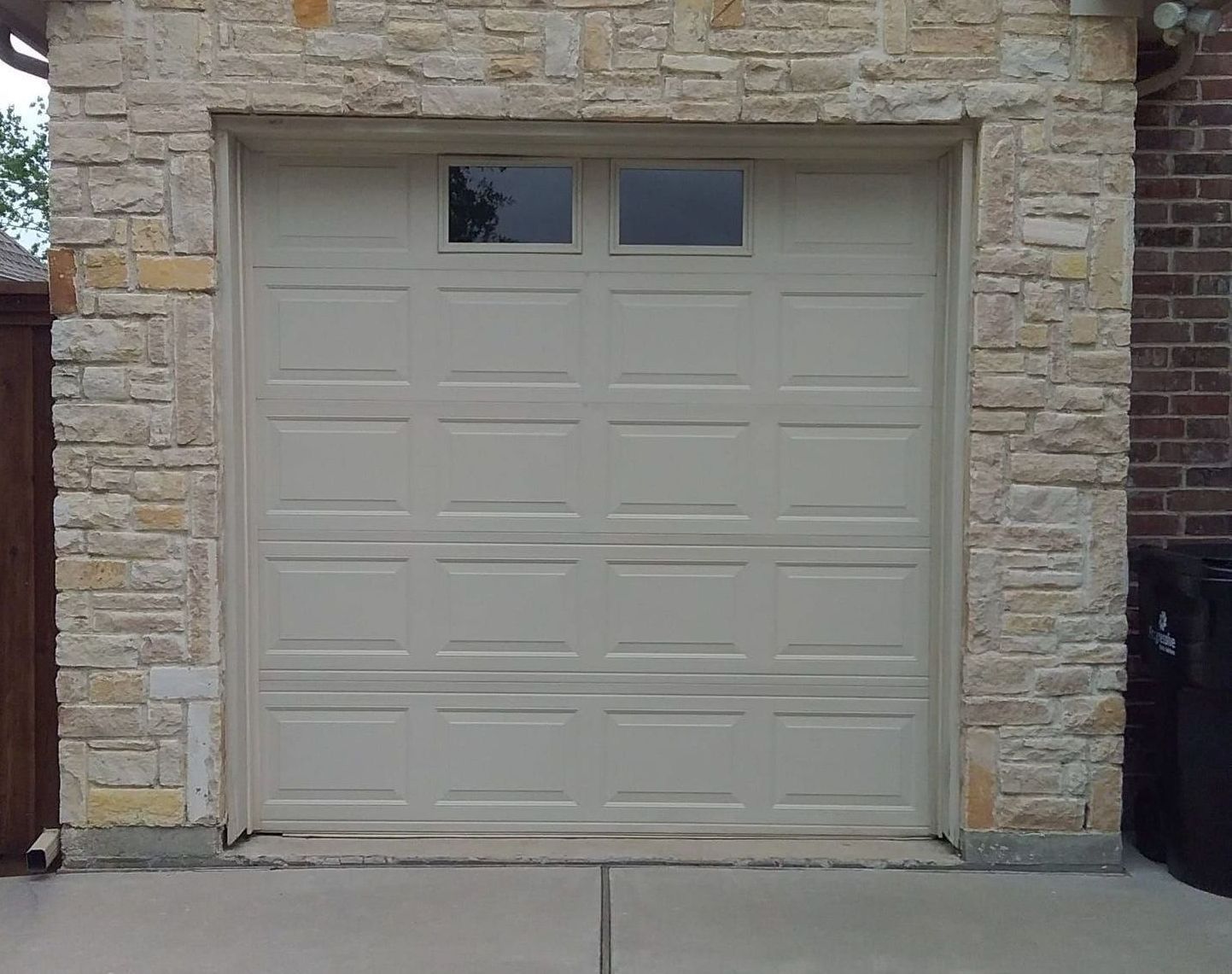 Tan garage door with two small windows, set in a stone wall.