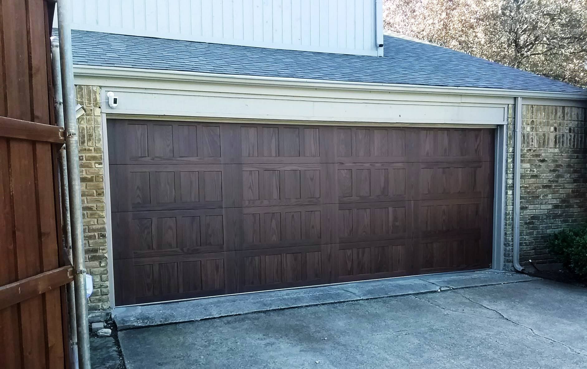 A dark brown, multi-paneled garage door installed on a beige brick residential garage with a light-colored roof.
