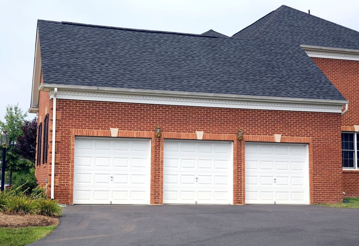 Brick building with three white garage doors under a dark gray roof.