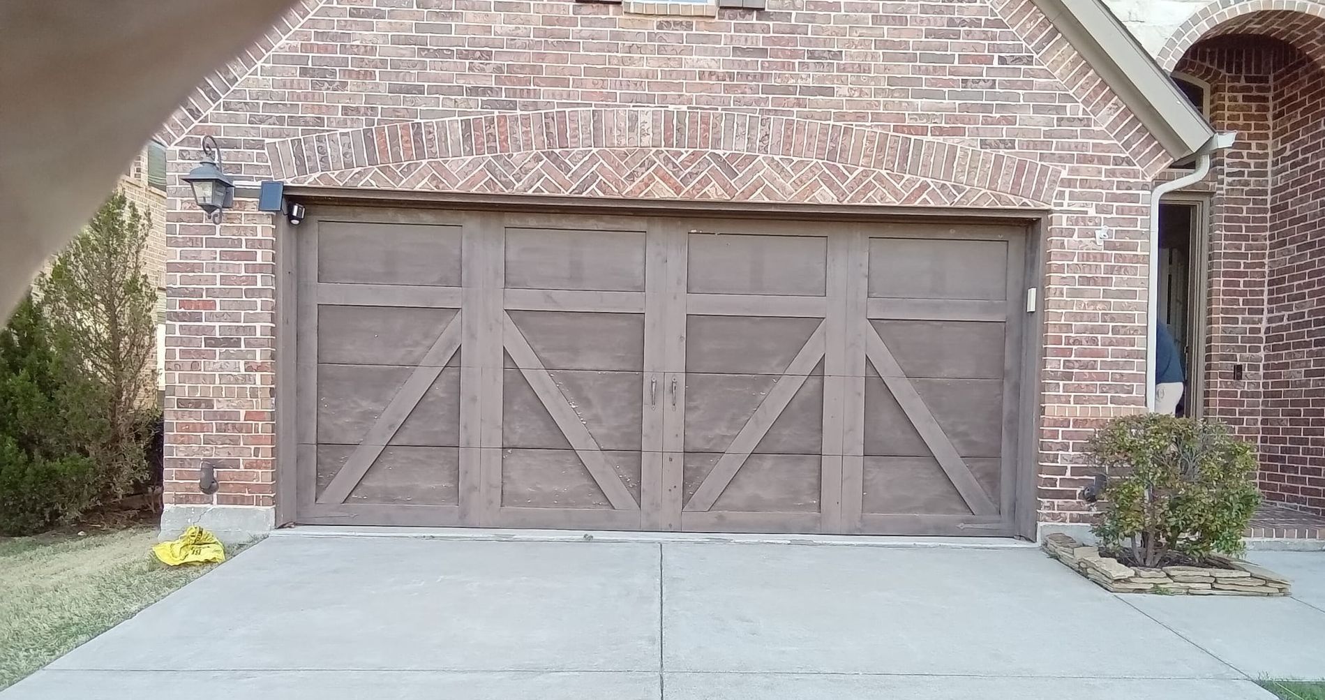 Brown garage door with diagonal accents, set in a brick facade, driveway in front.