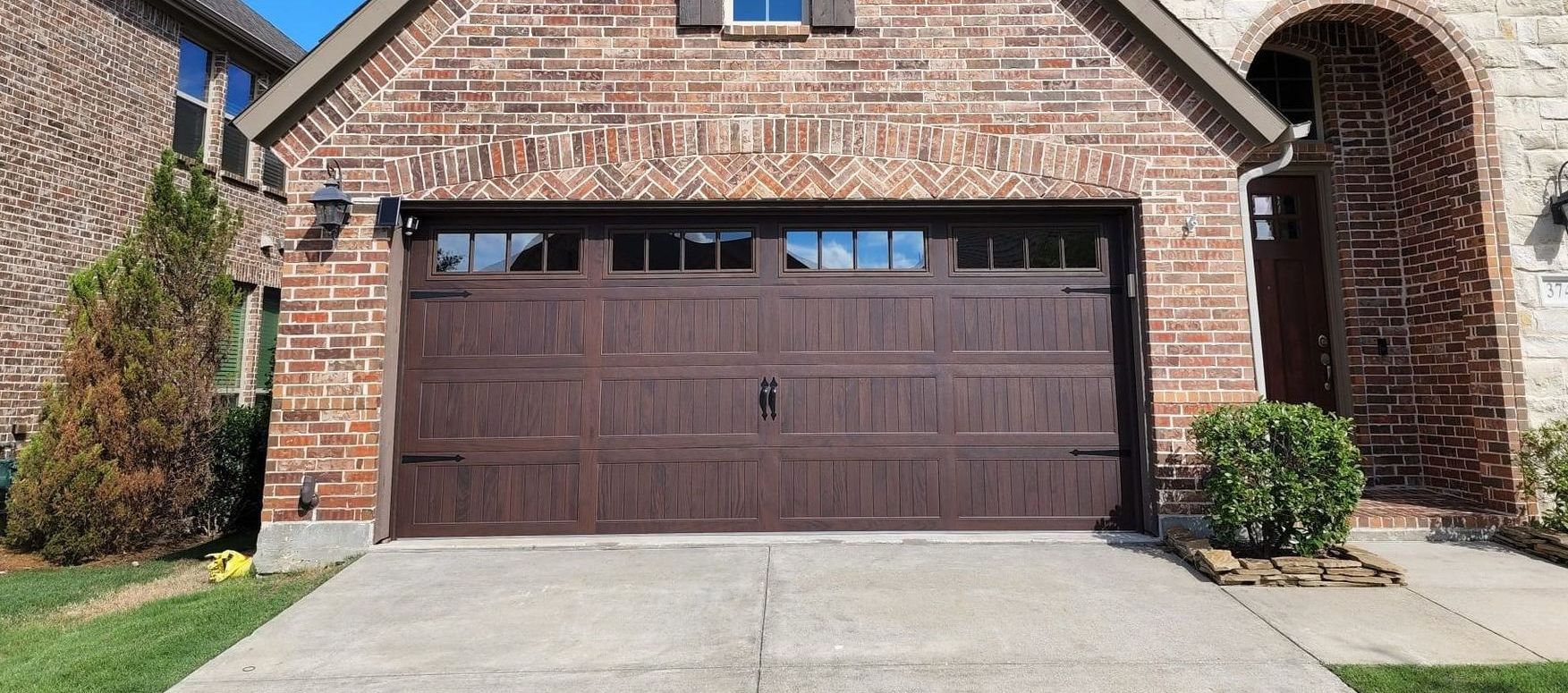 Brown garage door on a brick house with a concrete driveway.