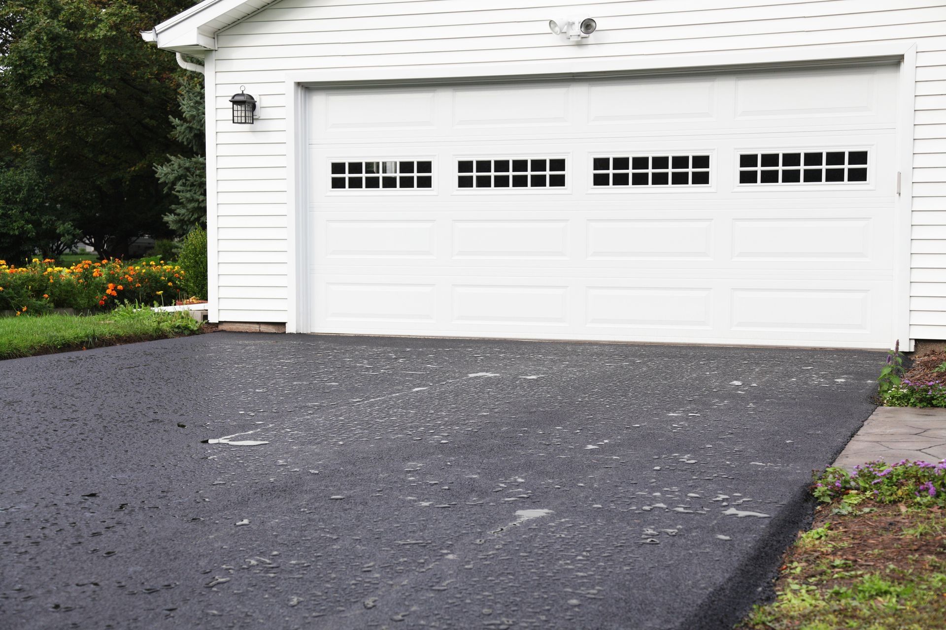 White garage door with windows, facing a black asphalt driveway.