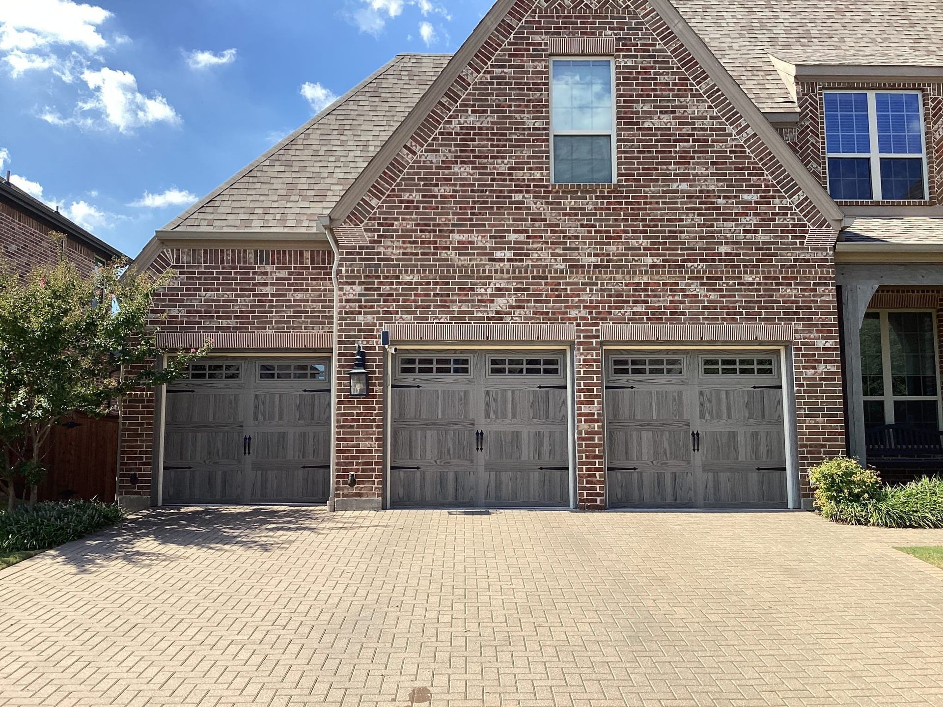 Brick house with three gray garage doors; brick paver driveway.