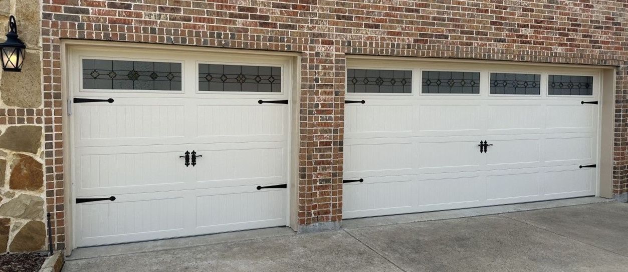 Two white garage doors with decorative black hardware, brick facade.