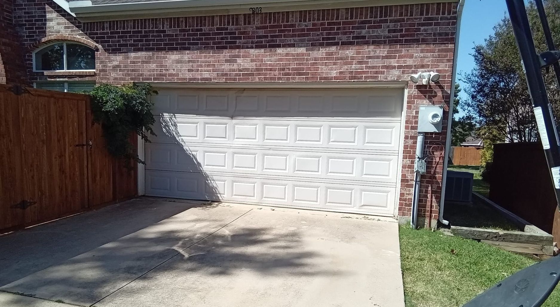 Garage with white door, brick exterior, driveway, wooden fence, and grass on the right.