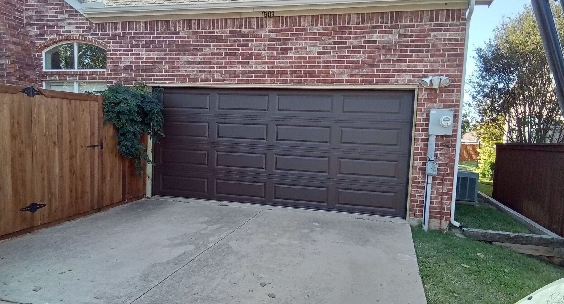 Brown garage door on brick building with a concrete driveway and wooden fence.