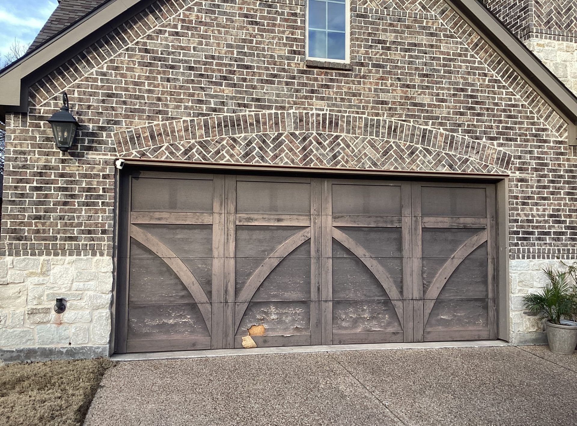 Brown brick facade with arched garage door, gravel driveway.