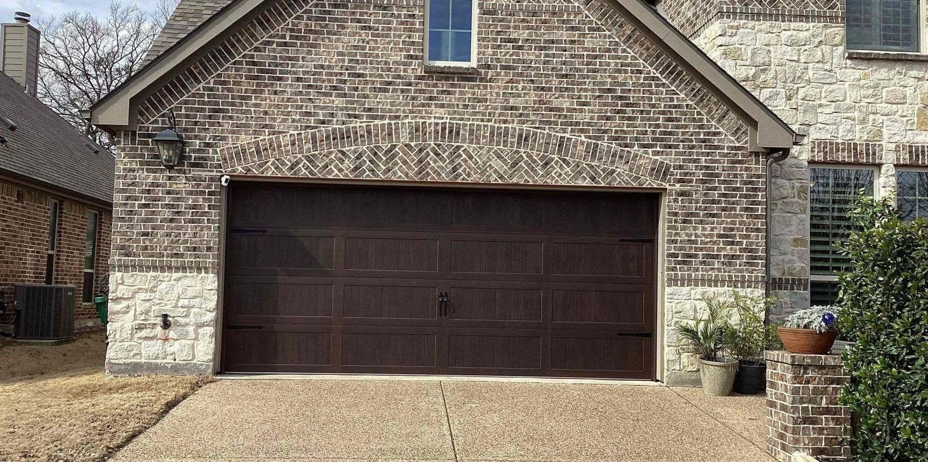 Brown brick home with a closed garage door. There is a gravel driveway and plants on the right.