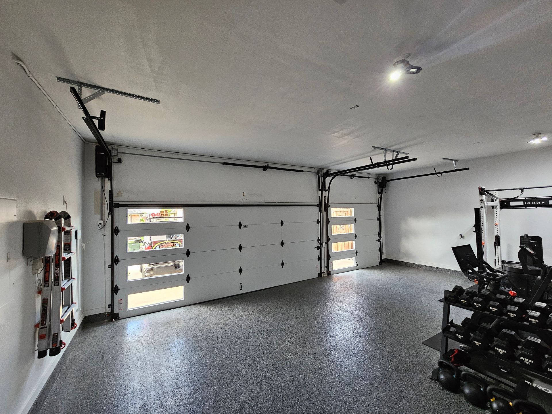 White garage with a gray speckled floor, door partially open. Gym equipment visible.
