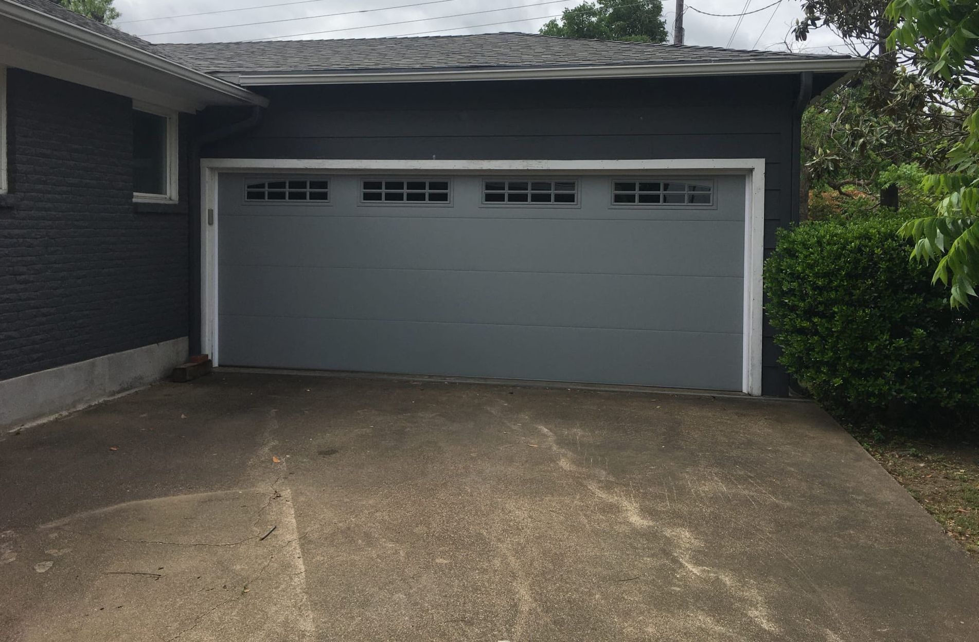 Gray garage door on a gray house, with a concrete driveway in front.