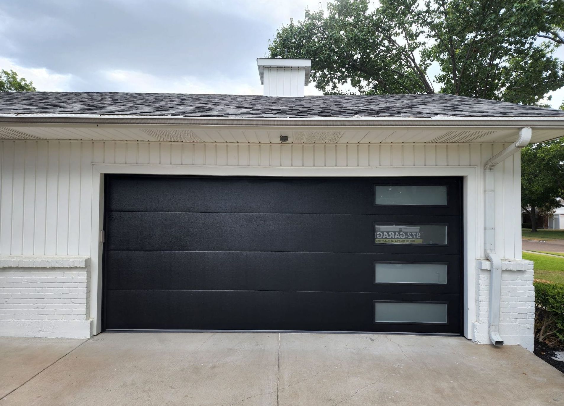 Black garage door with frosted glass windows. White building, concrete driveway.