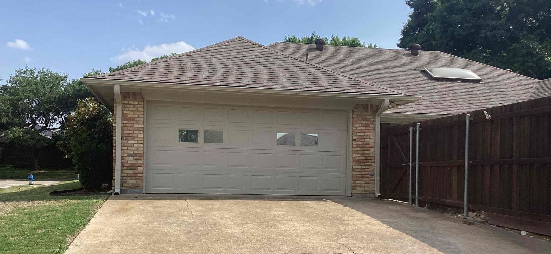 Garage with a light-colored door, stone accents, and a brown roof, with a driveway and green grass.
