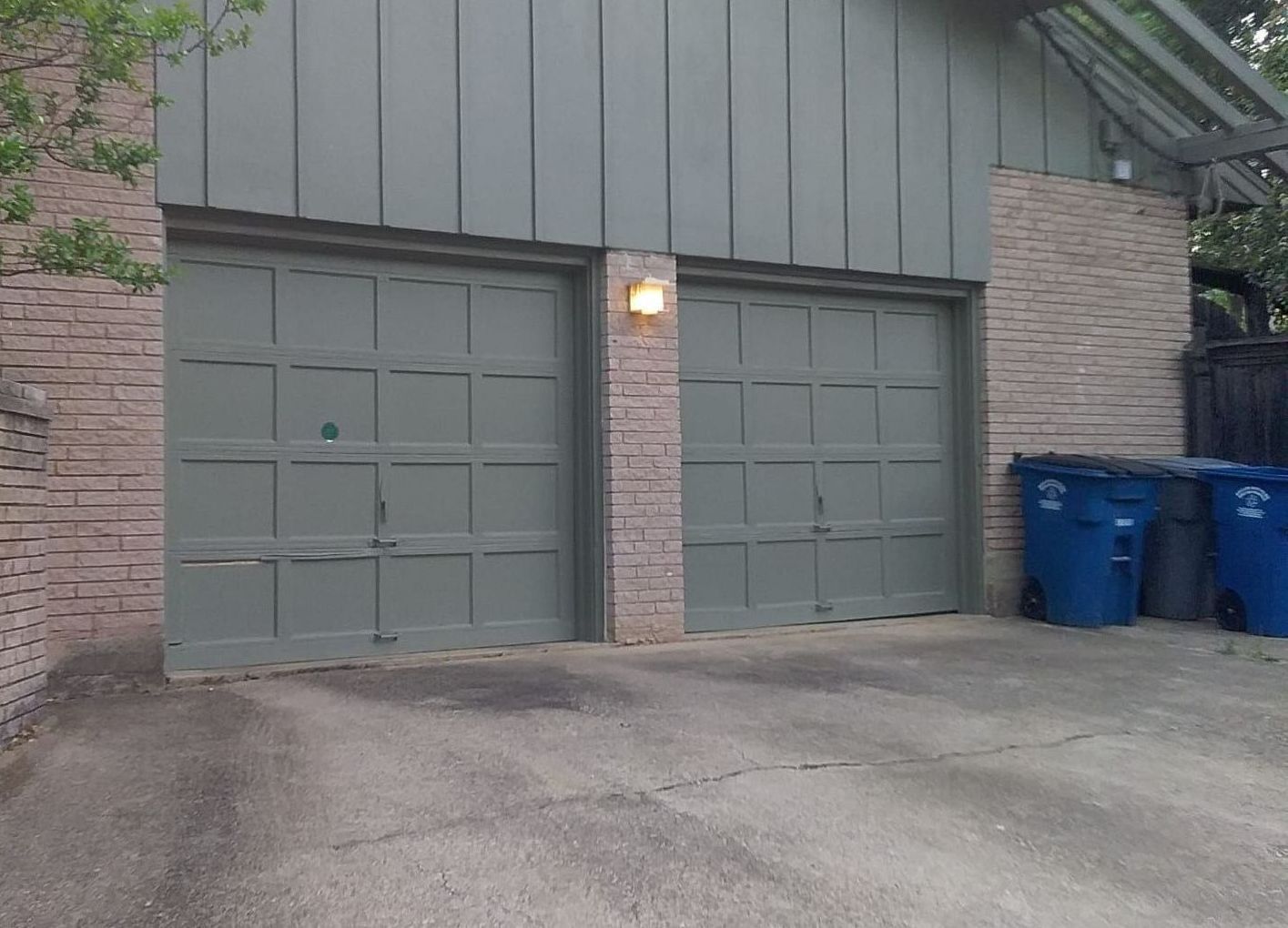 Two gray garage doors, brick exterior, blue trash cans.