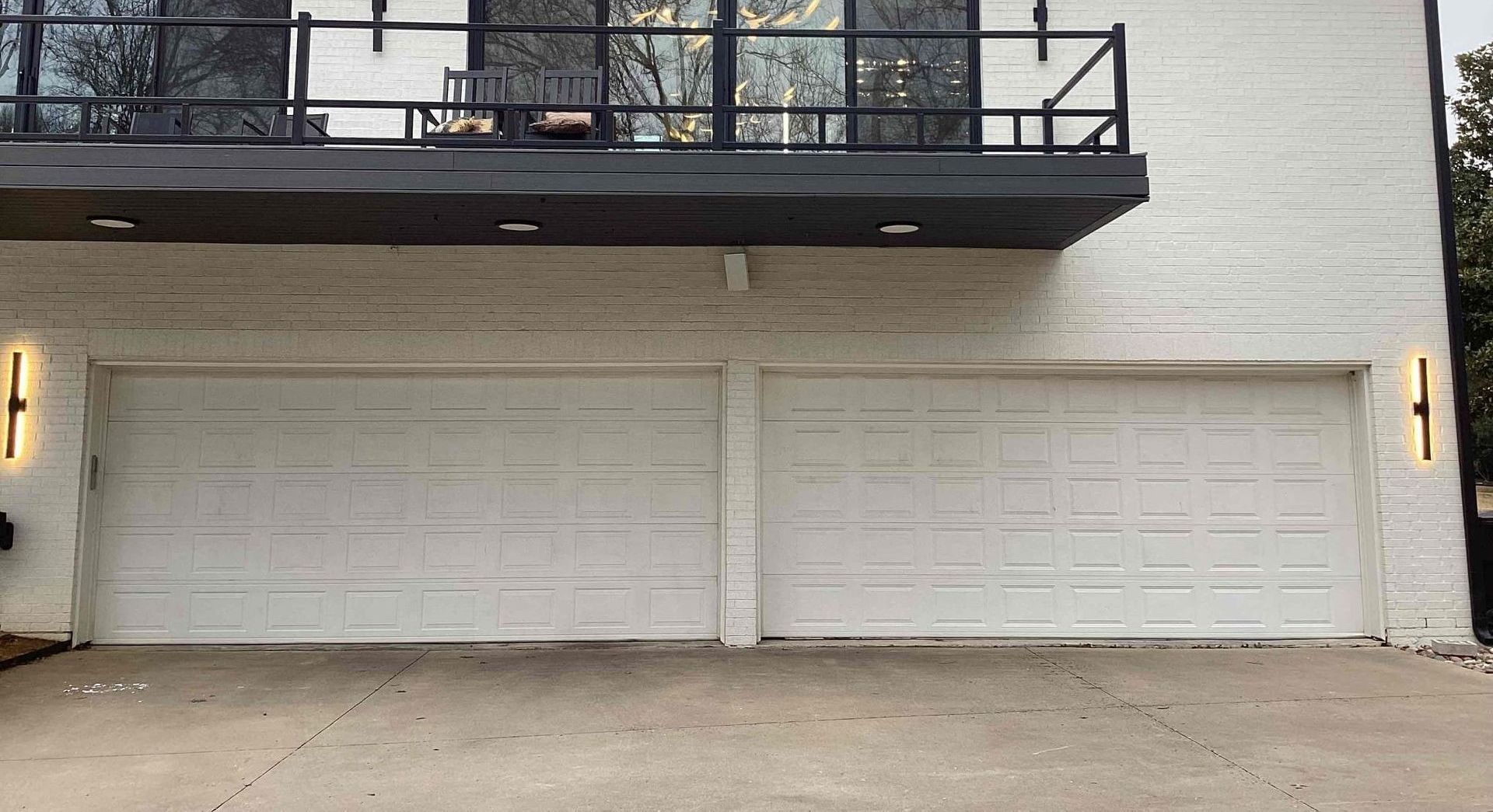 White garage doors on a two-story building with a balcony above.