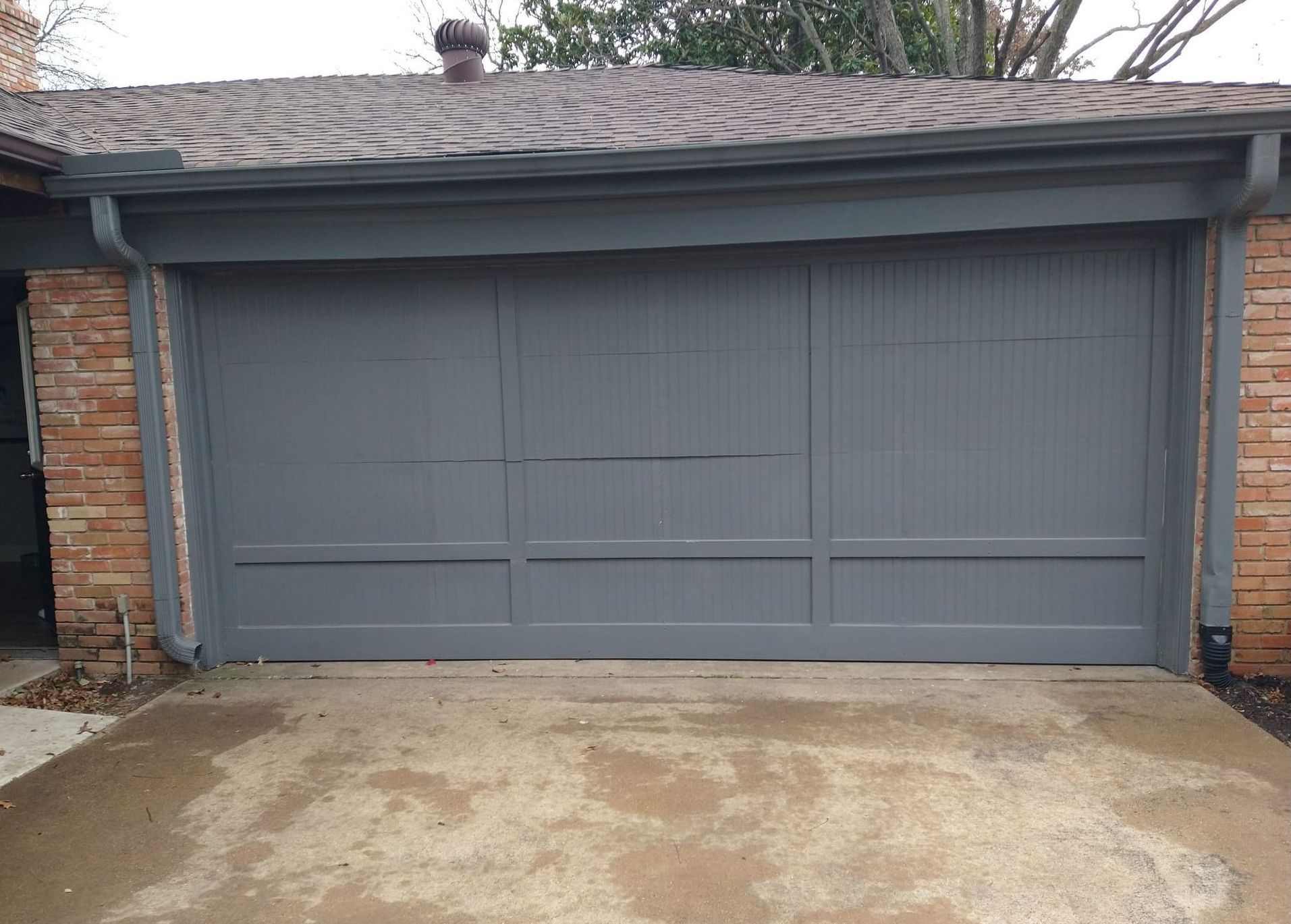Gray garage door with brick trim, set on concrete driveway.