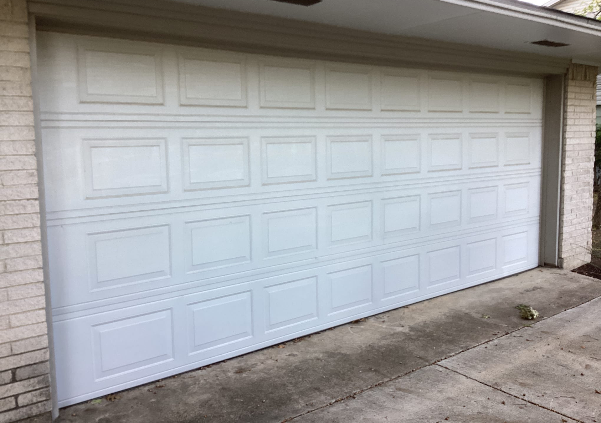 White panel garage door on a house with a concrete driveway and brick siding.