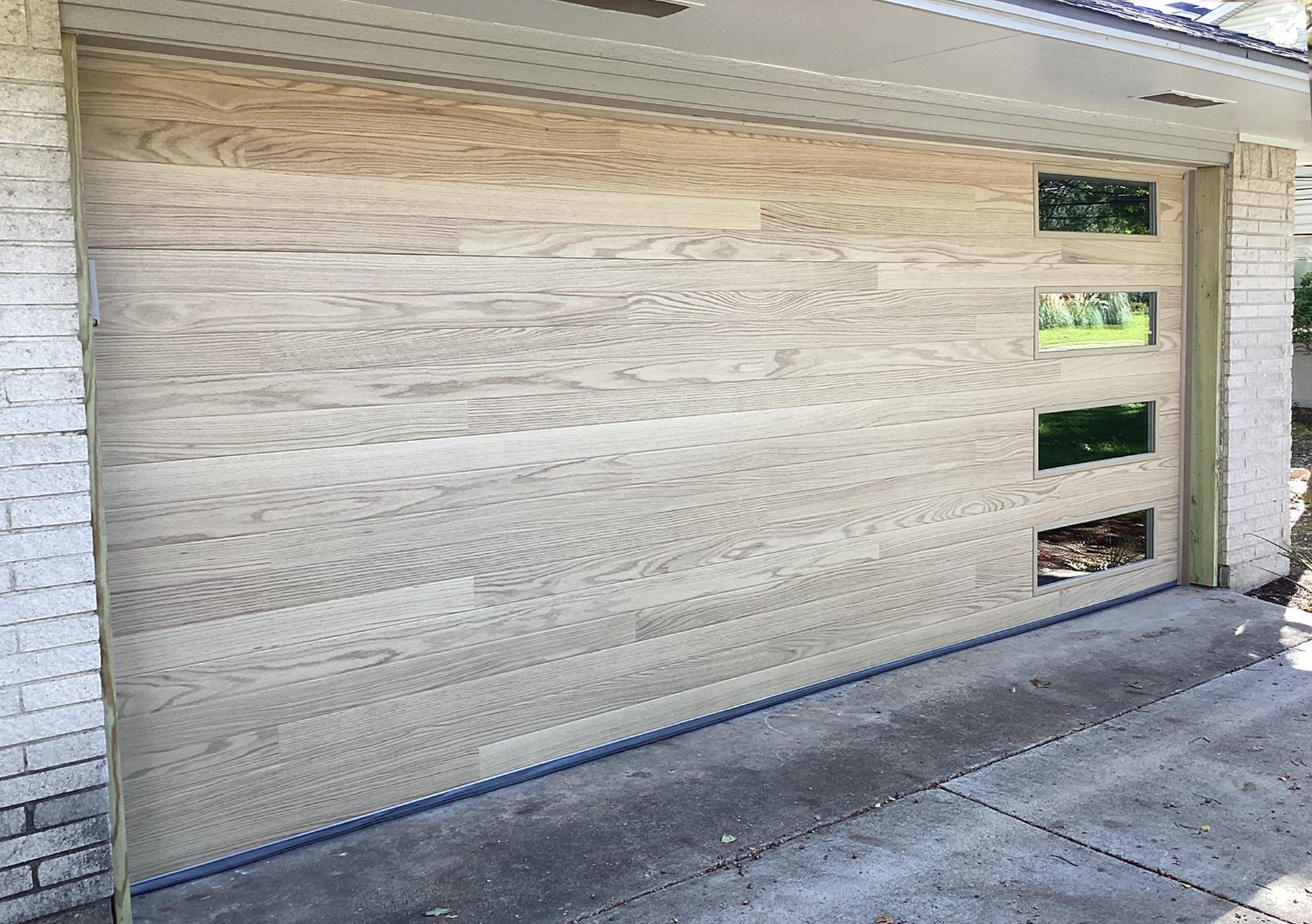 Wooden garage door with three square windows, installed in a brick house.