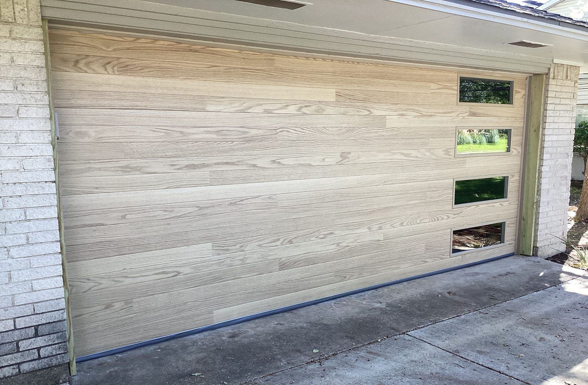 Wooden garage door with three square windows, installed in a brick house.