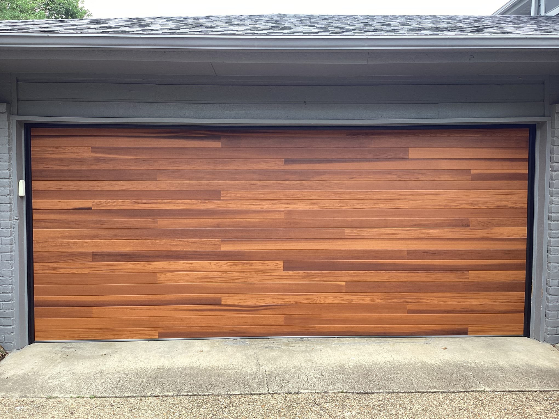 Wooden garage door with horizontal planks, set in a gray frame and against a gray house.