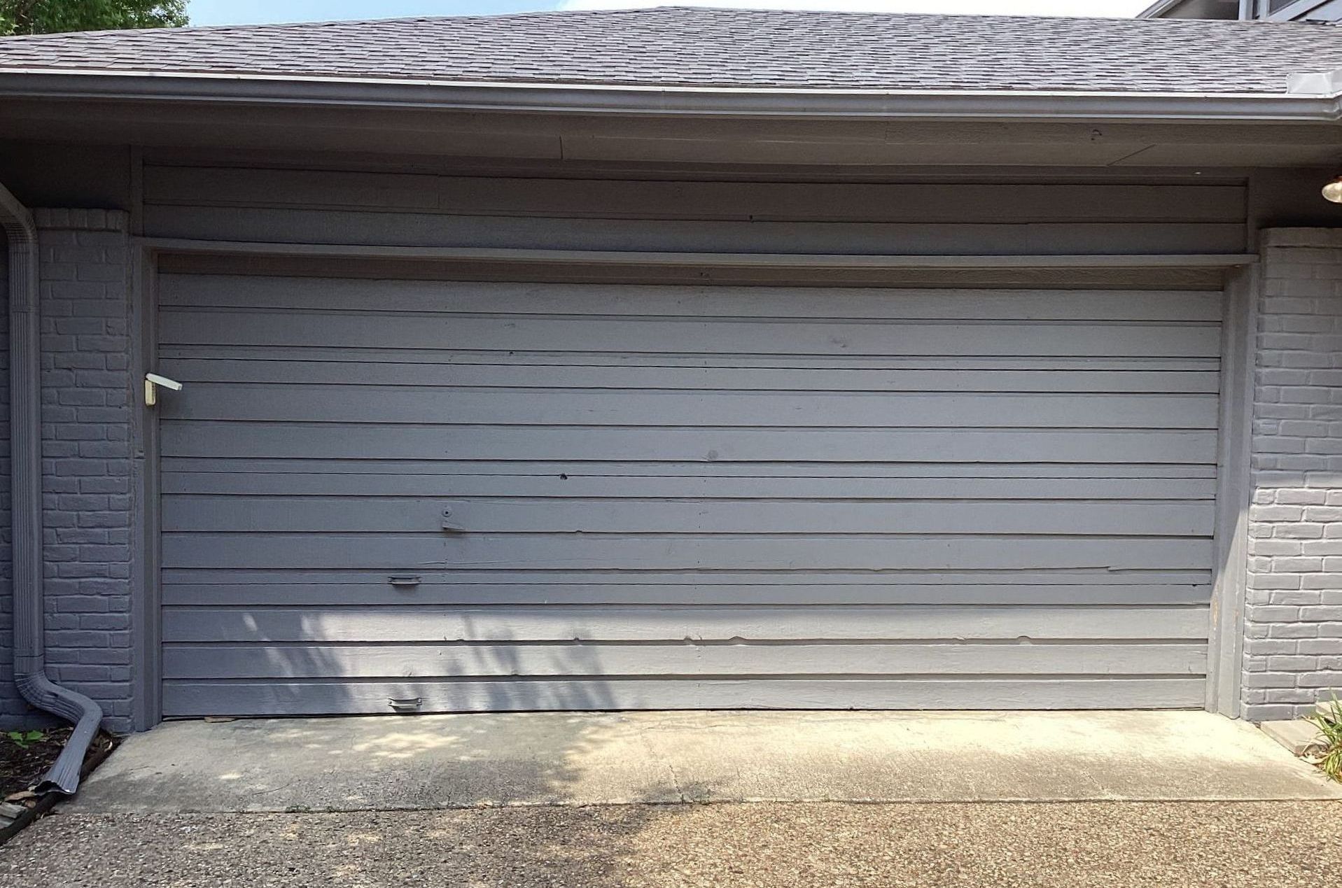 Gray wooden garage door with weathered paint and a stone driveway.