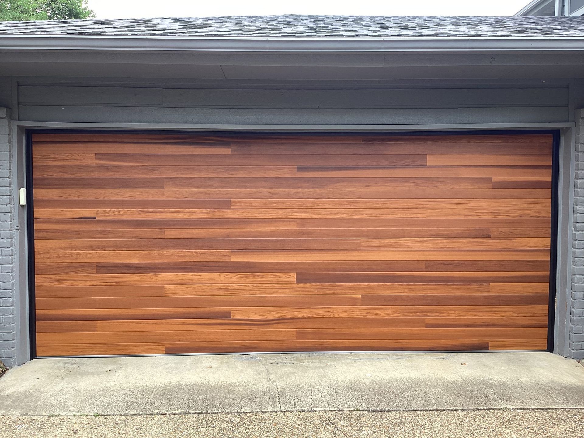 Wooden garage door with horizontal planks, set in a gray frame and against a gray house.
