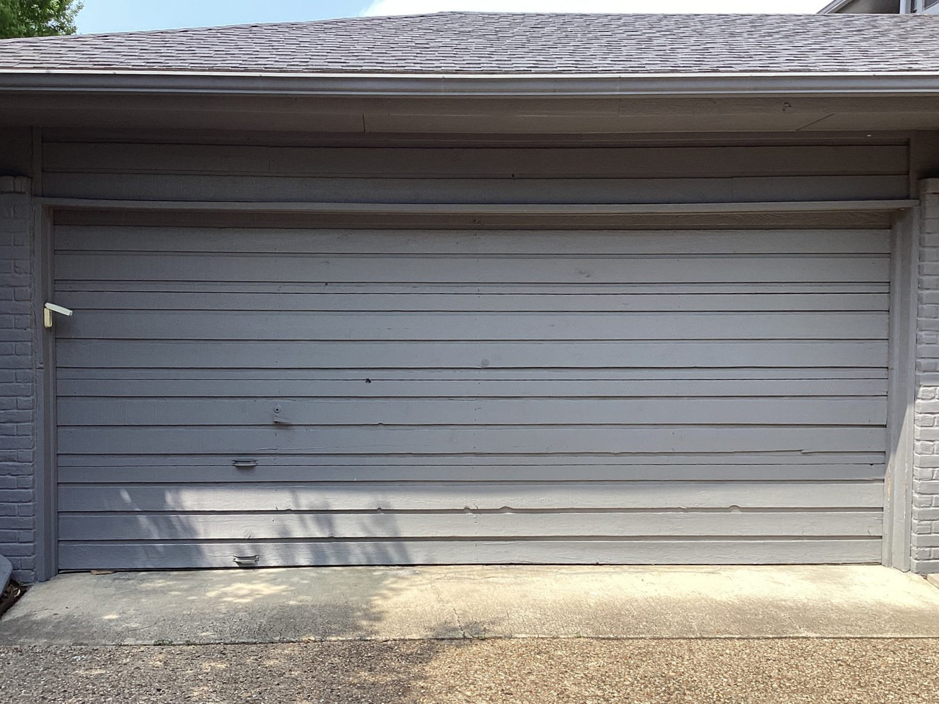 Gray wooden garage door with weathered paint and a stone driveway.