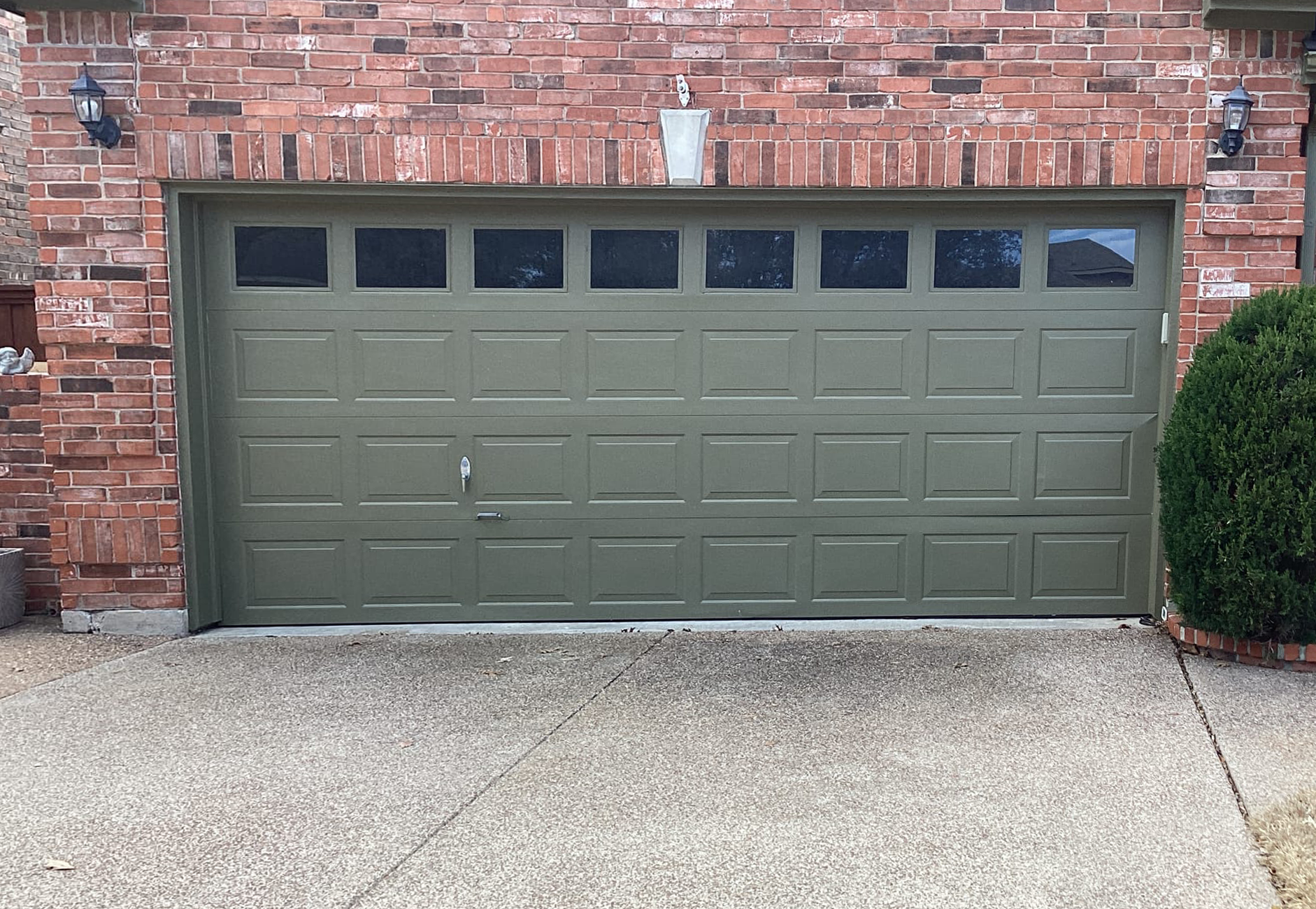 Green garage door with windows, in a brick building; concrete driveway.
