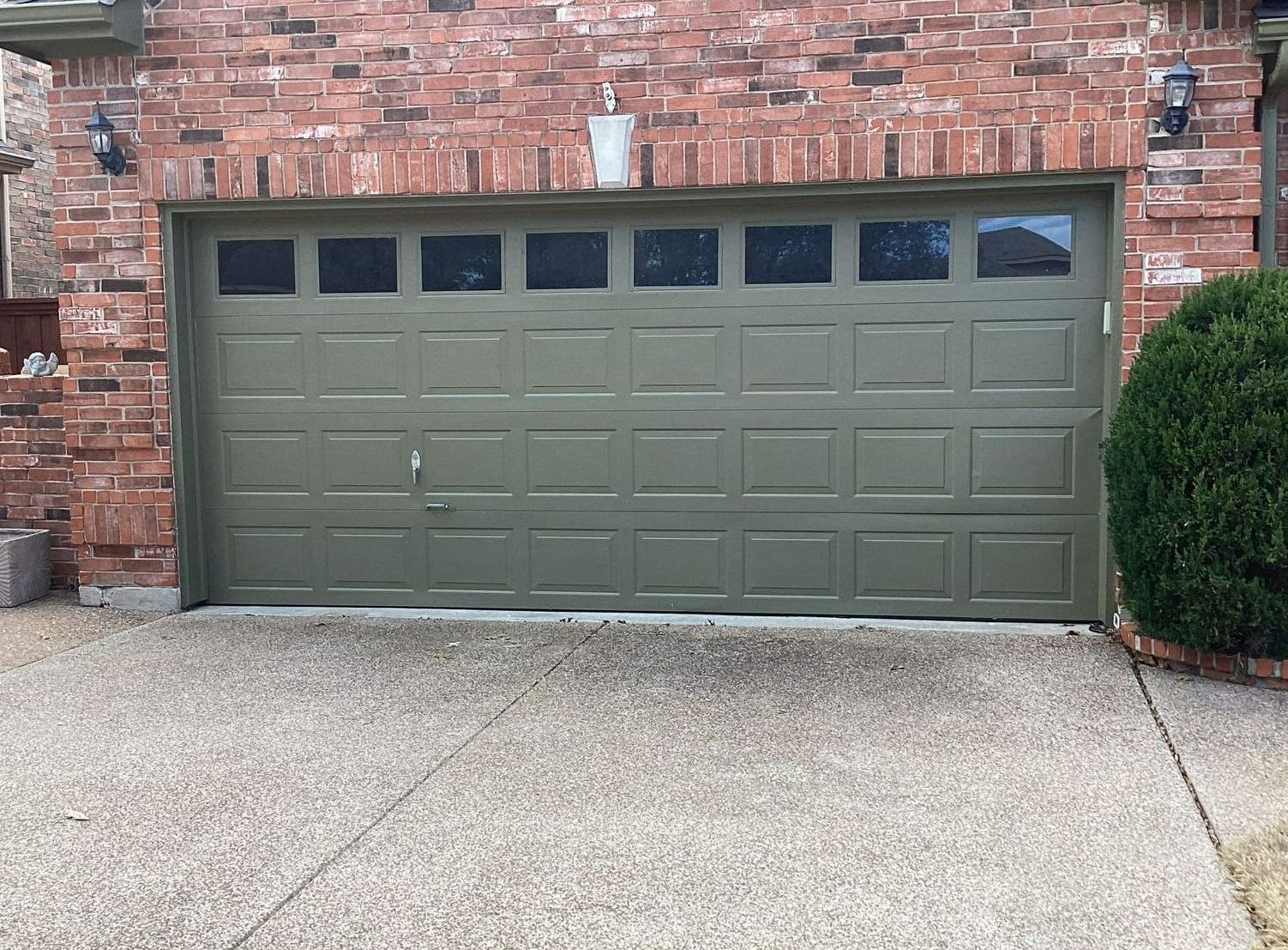 Green garage door with windows, in a brick building; concrete driveway.