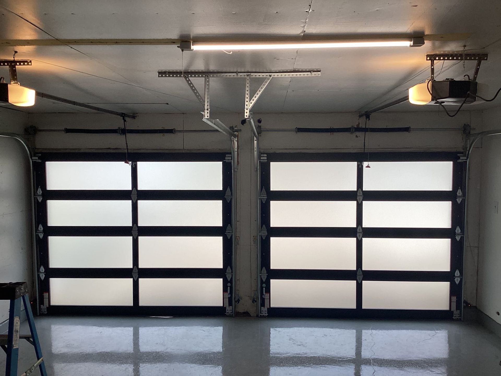 Two glass garage doors with black frames in a garage, overhead lighting.