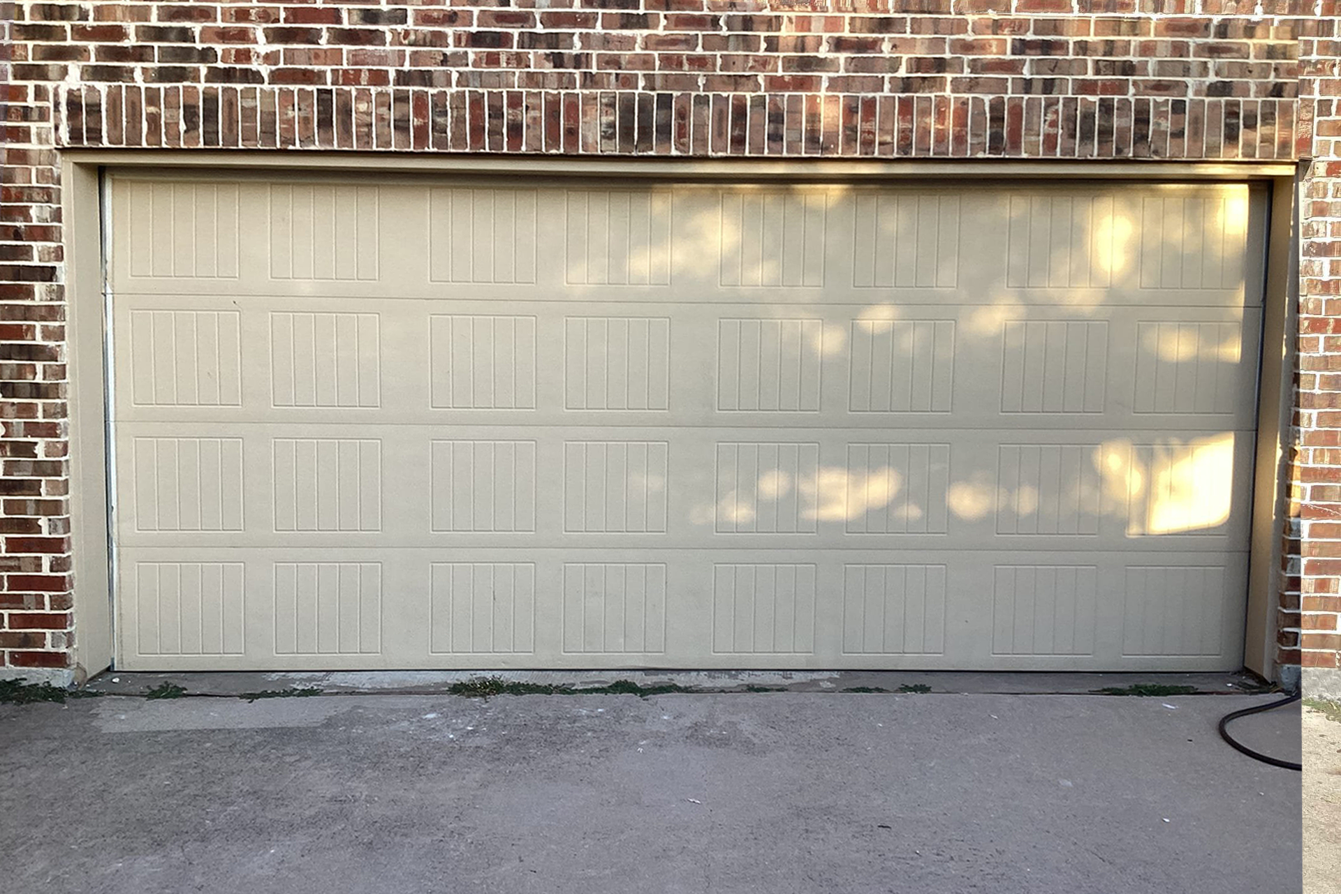 Tan garage door below brick wall; sunlight casts shadows.
