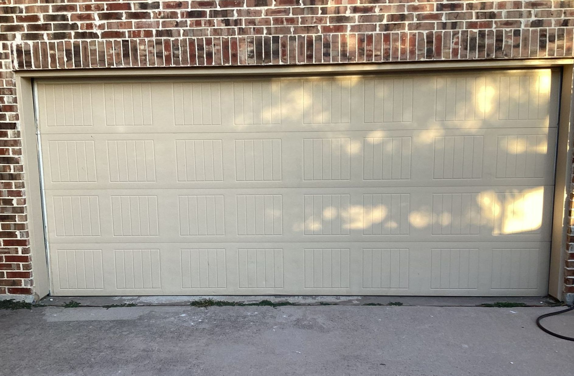 Tan garage door below brick wall; sunlight casts shadows.