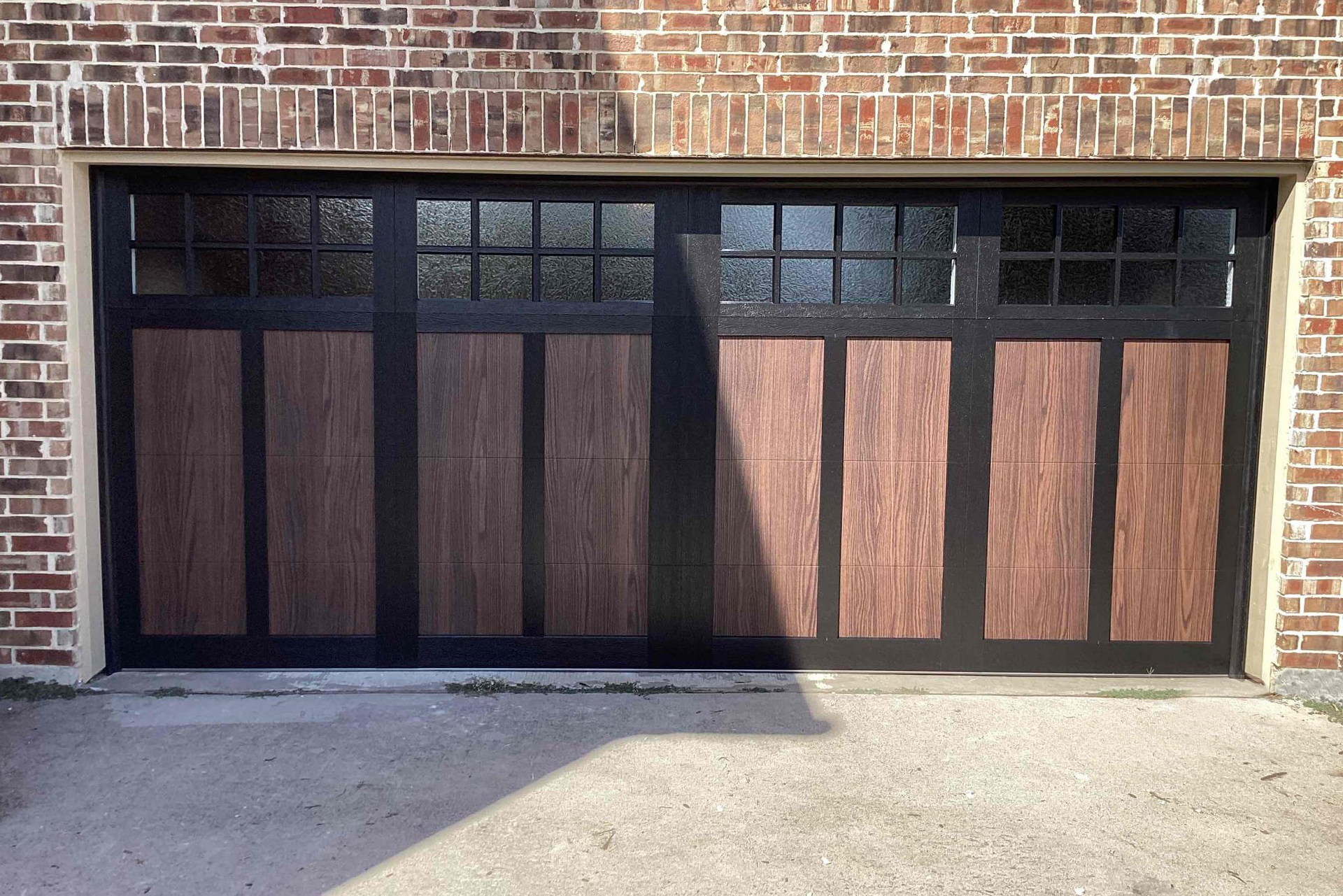 Brown and black garage door with windows, set in a brick building.
