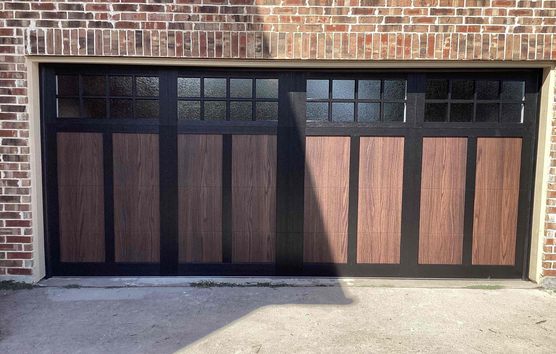 Brown and black garage door with windows, set in a brick building.