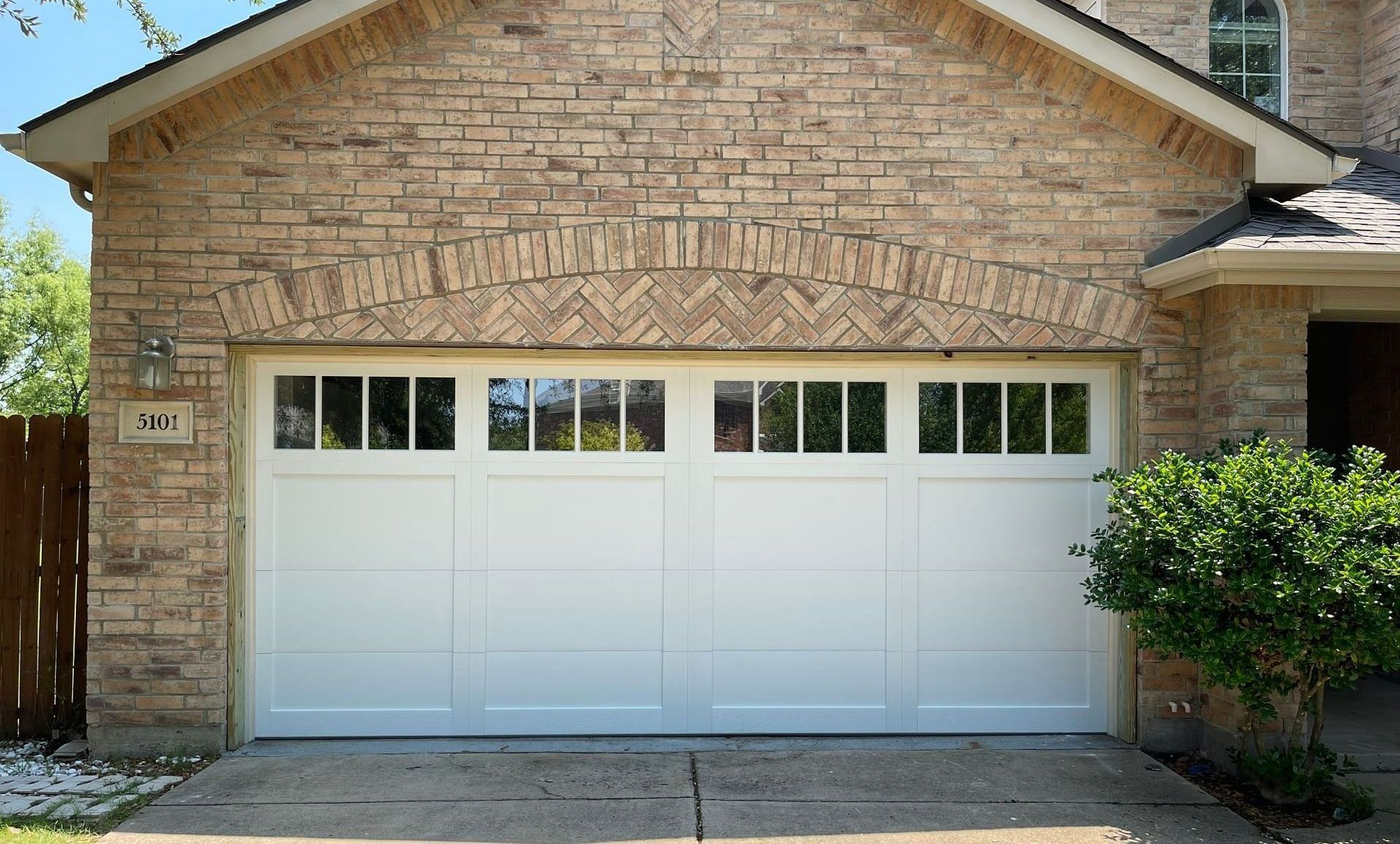 White garage door with window panels, in front of a brick facade.