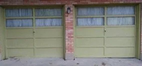 Two green garage doors with windows, separated by a brick column, beneath a brick roof.