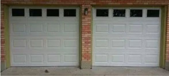 Two white garage doors with rectangular windows above, flanked by brick walls.