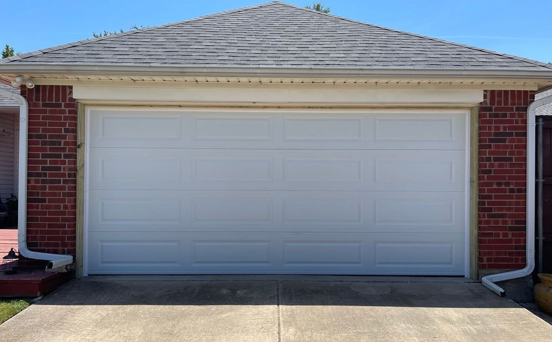 White garage door framed by red brick, under a weathered roof.
