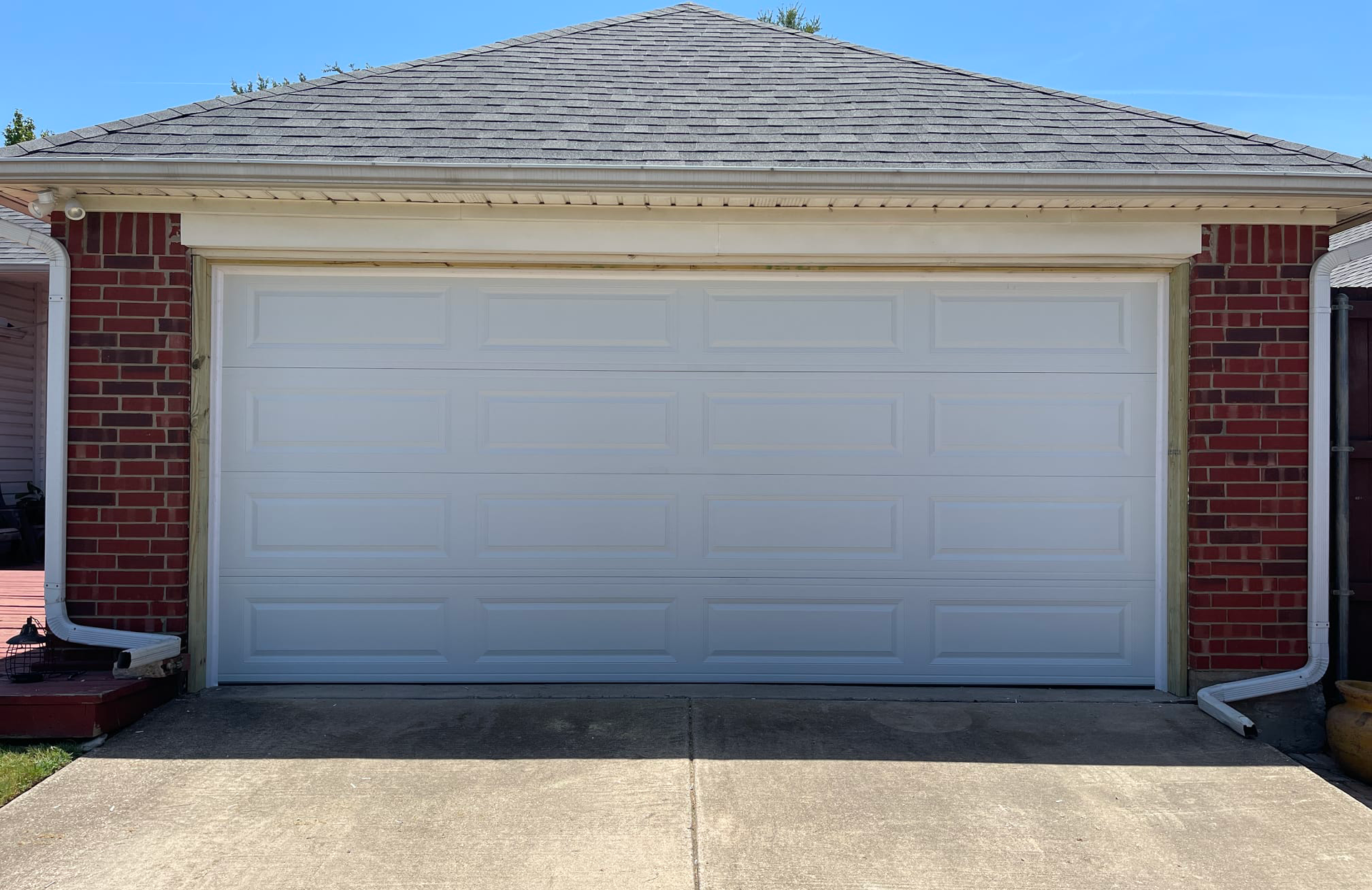 White garage door framed by red brick, under a weathered roof.