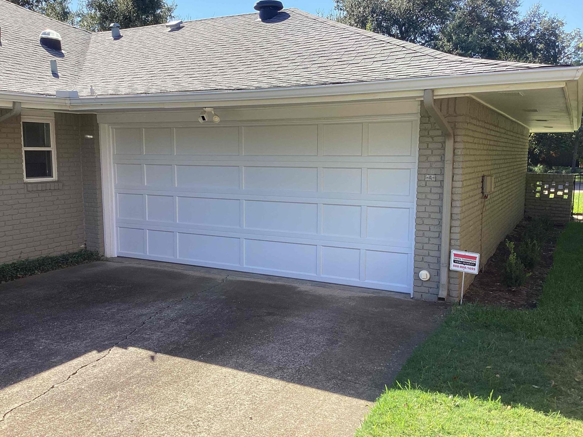 White garage door on a brick house with concrete driveway and green lawn.