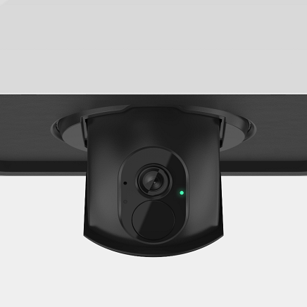 Black security camera mounted on a black surface, with a green light illuminated.