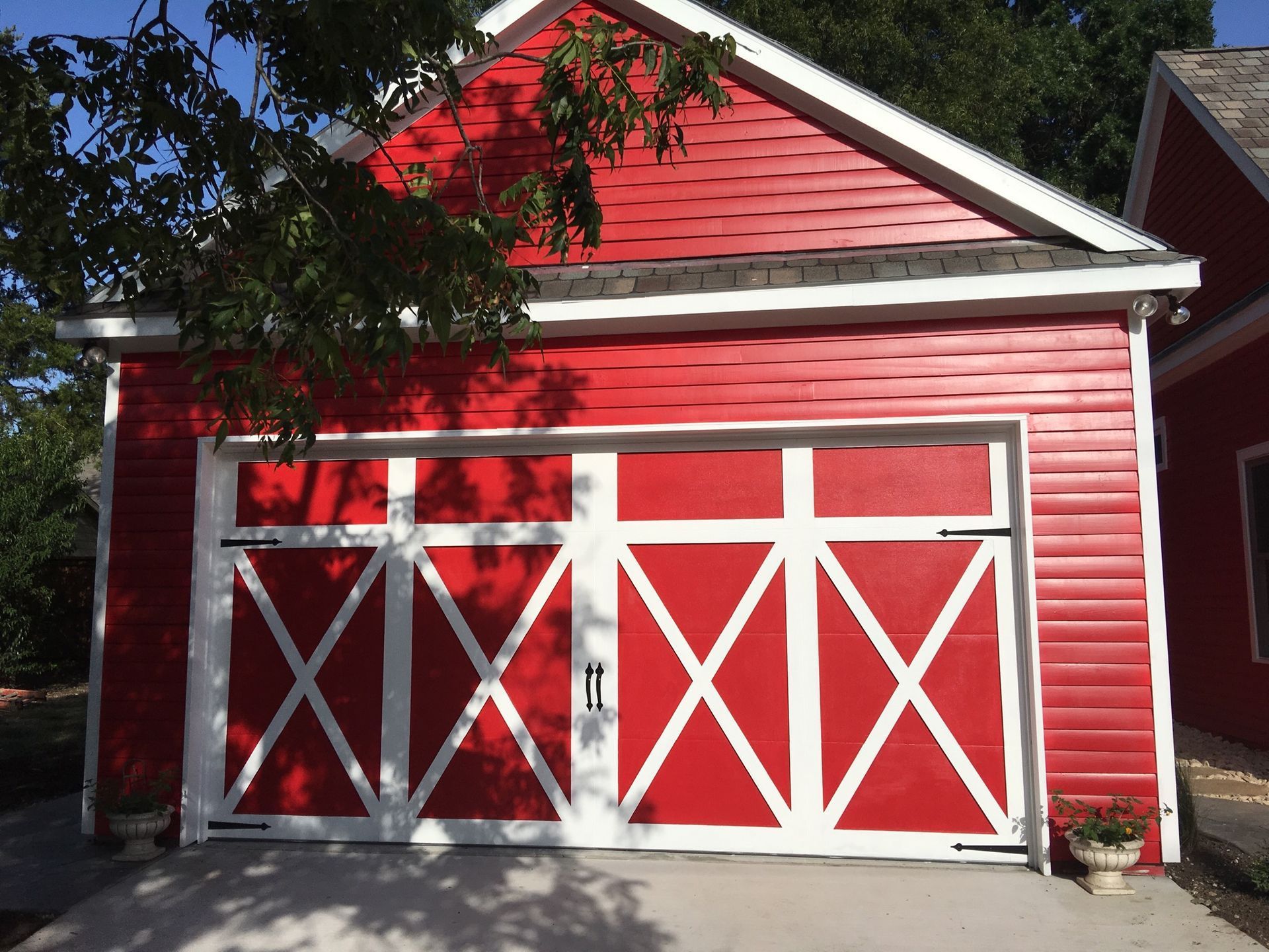 A vibrant red detached garage with white trim and a distinctive cross-patterned double door.