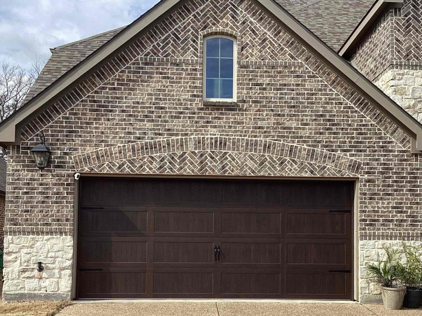 Brown brick house with a brown garage door and arched window.