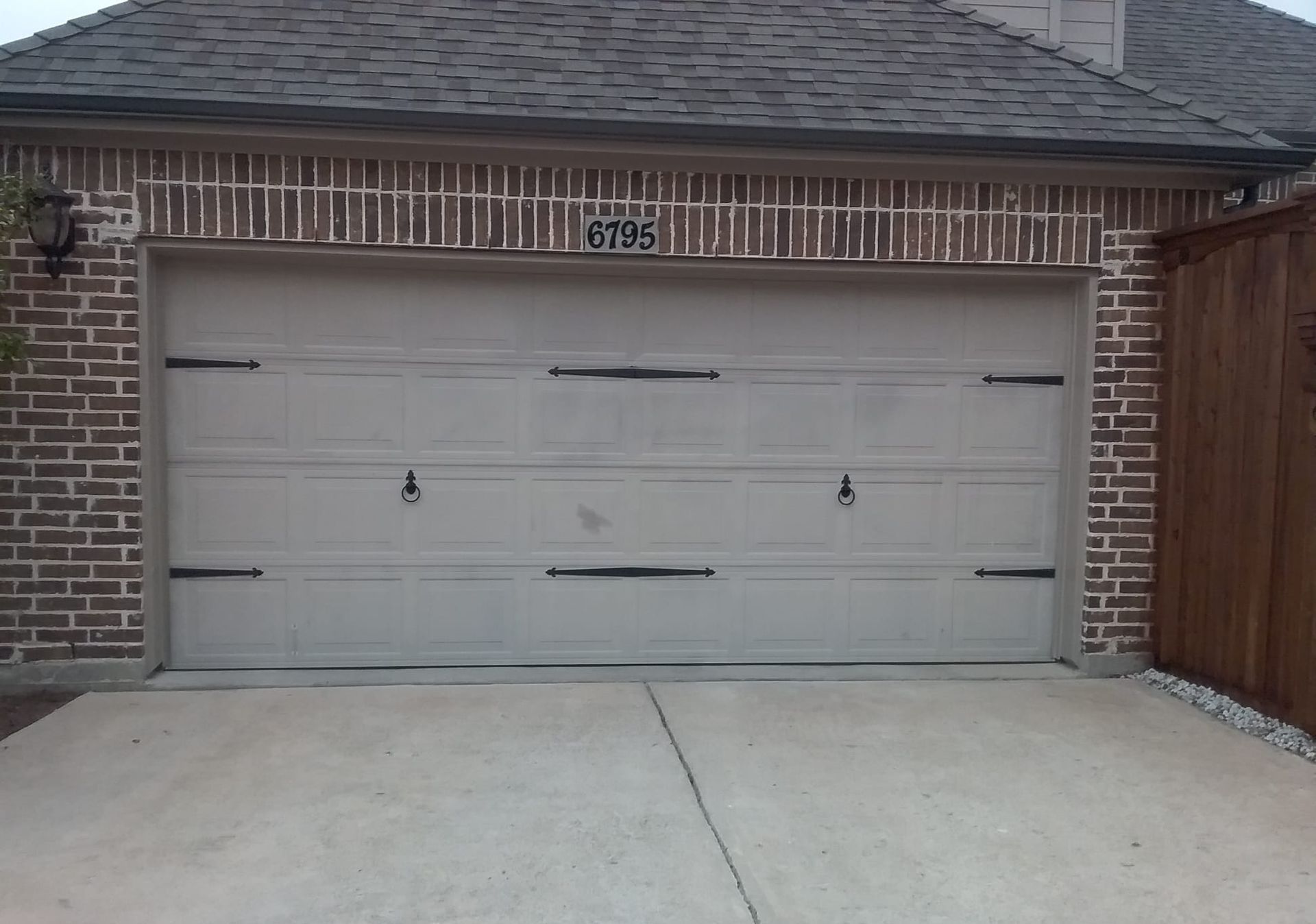 Garage door with decorative hardware, set in a brick facade, driveway in front.