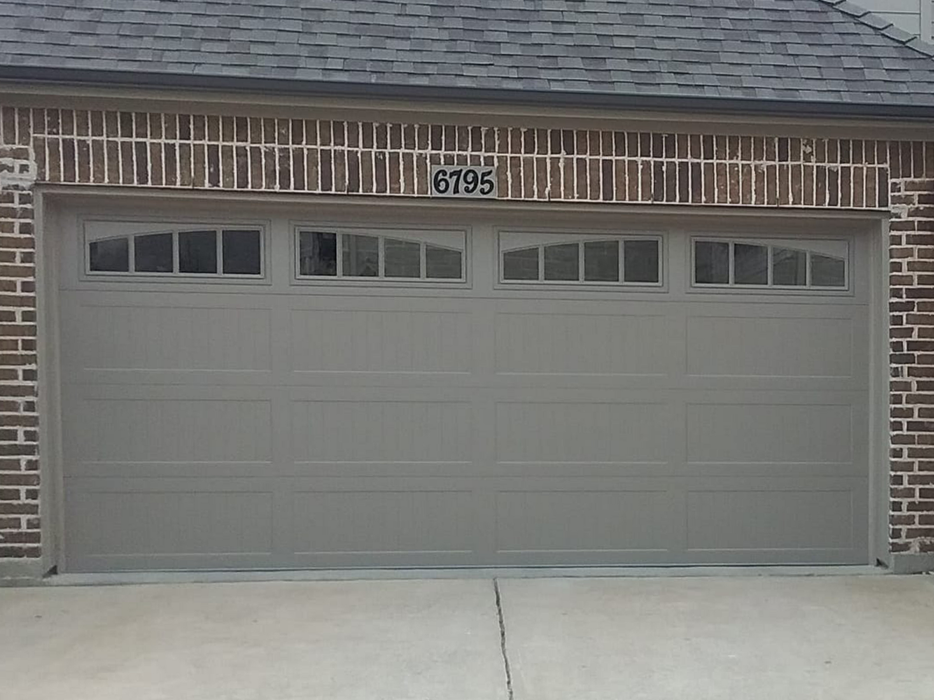 Gray garage door with brick facade, asphalt driveway.