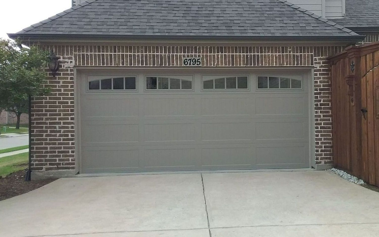 Gray garage door with brick facade, asphalt driveway.