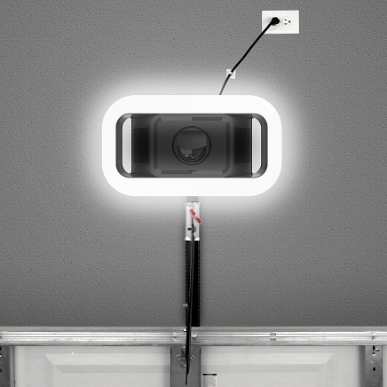 Garage door opener with illuminated frame, plugged into wall outlet.