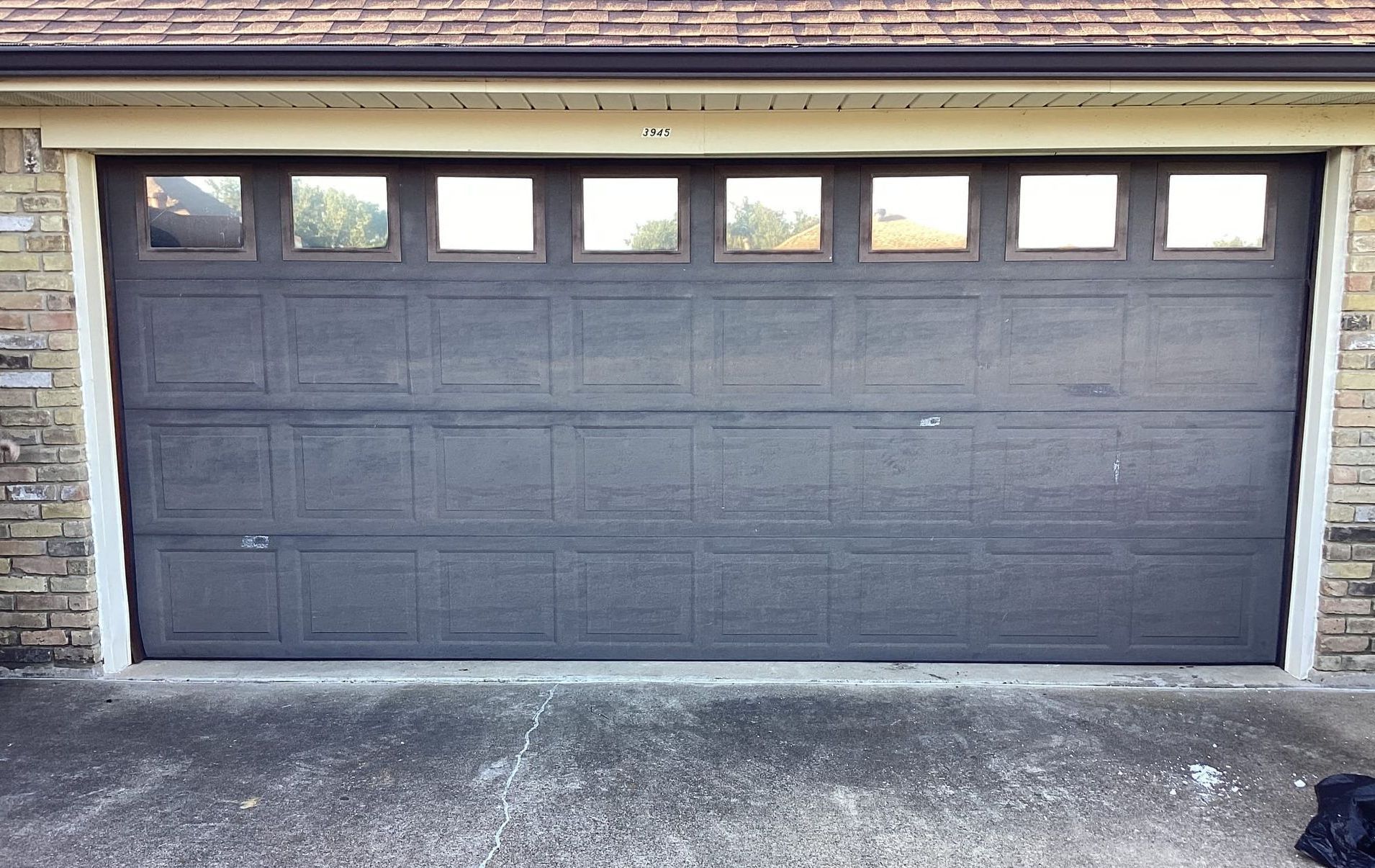 Gray garage door with window panels, in front of a brick building.