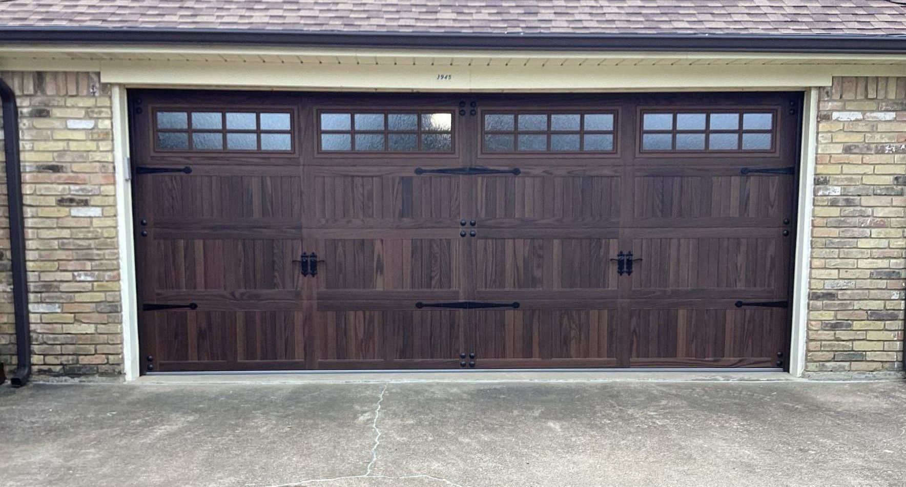 Brown garage door with decorative hardware and window panels. Brick building.